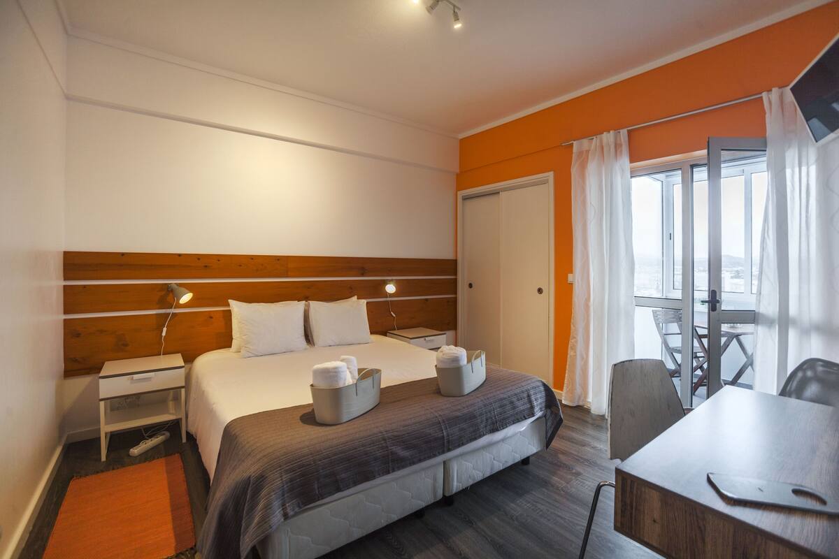 A modern hotel room with a large bed, bedside tables, a desk, and a balcony with a view.