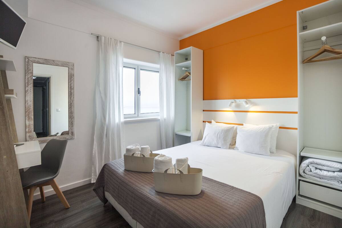 A hotel room with a bed, a desk, a chair, a wardrobe, and a window with curtains.