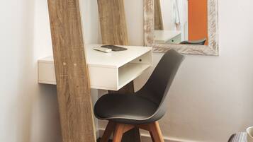 Una habitación moderna con un escritorio blanco, una silla negra y un espejo que refleja un baño con una pared de acento naranja.