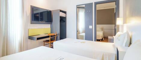 Habitación de hotel con dos camas, un escritorio, un televisor y un baño visible a través de una puerta abierta.