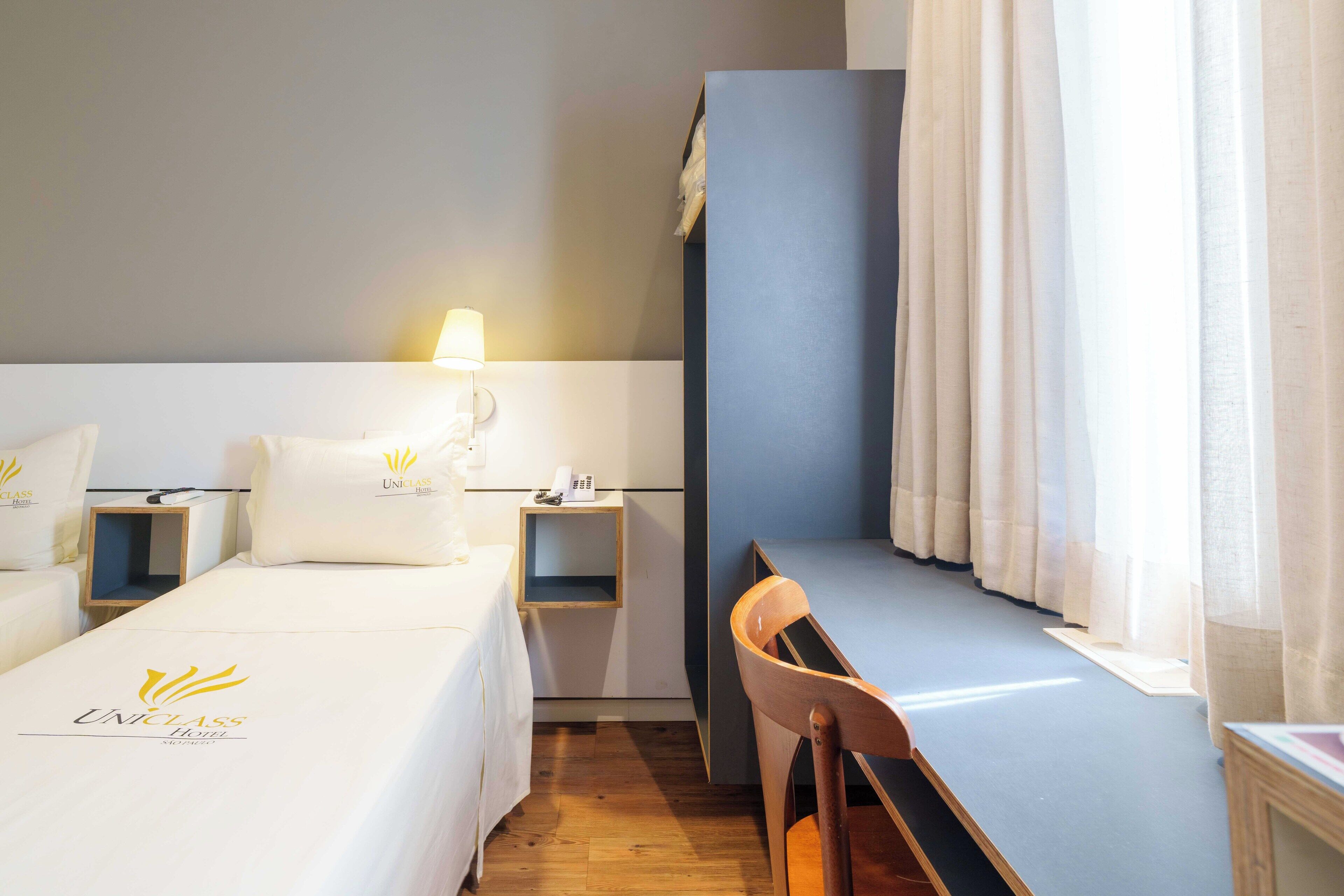 A hotel room with two beds, a desk, and a chair. There is a lamp on the desk and a phone on the nightstand.