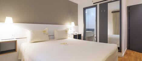 A hotel room with a large bed, bedside lamps, a wardrobe, and an air conditioning unit.