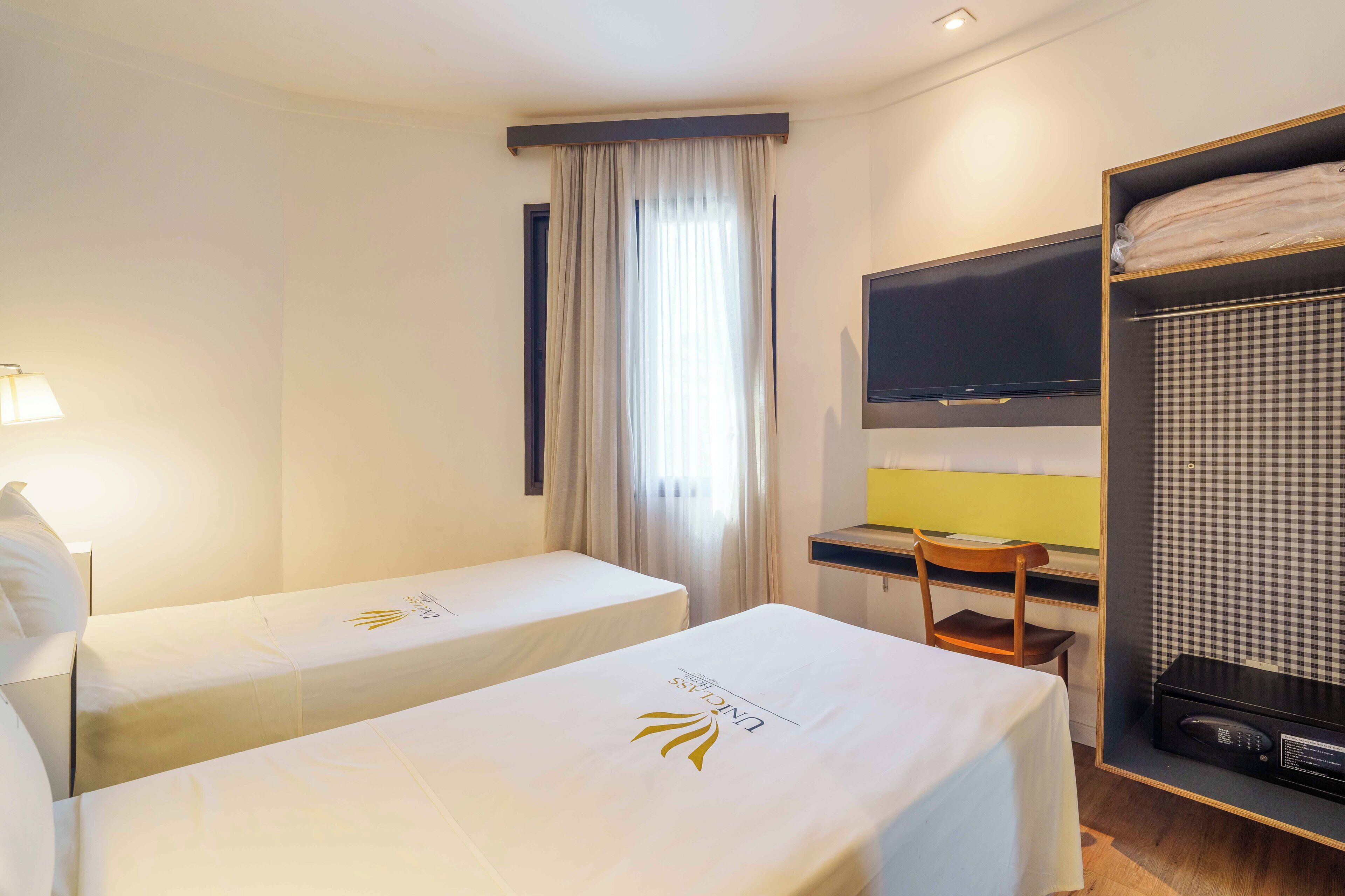 A hotel room with two single beds, a desk, a chair, a TV, and a microwave.