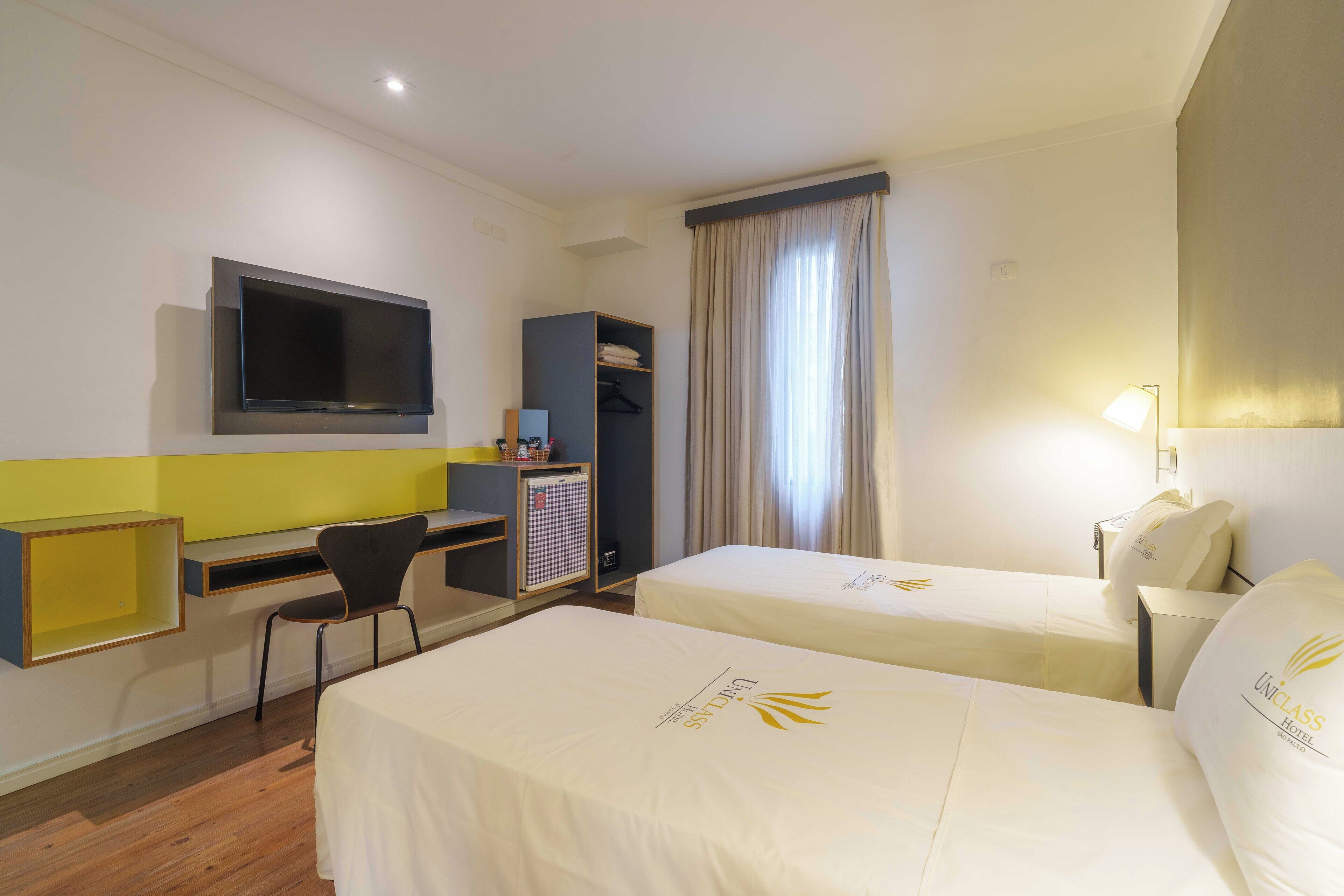 Habitación de hotel con dos camas, un escritorio, una silla, un televisor y un armario.