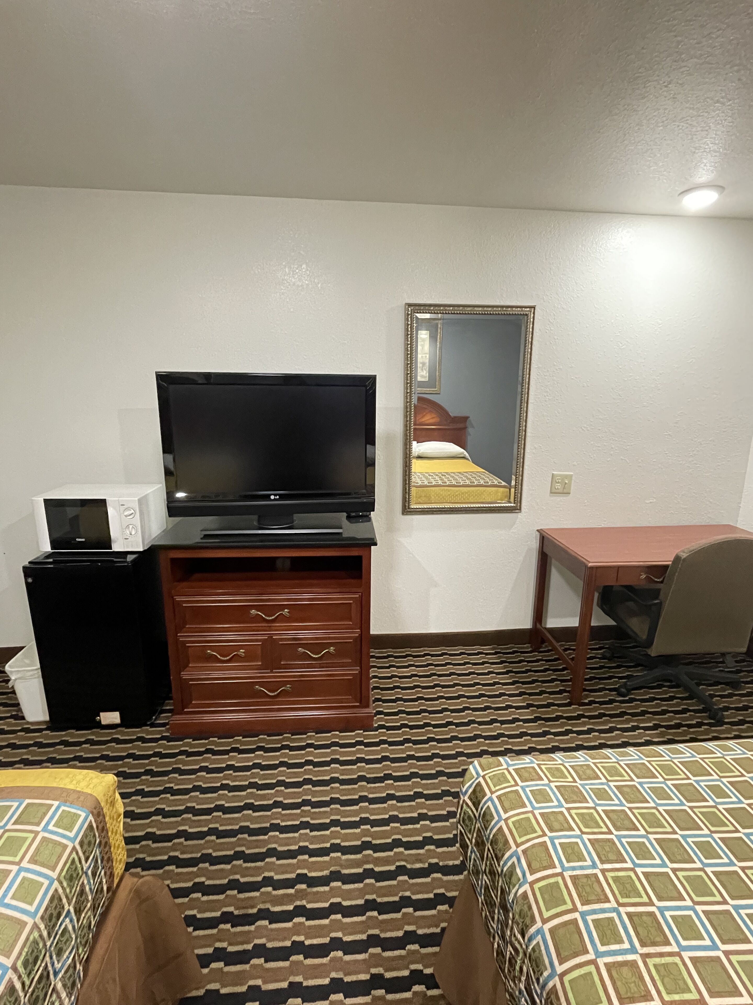 A hotel room with a television, a microwave, a wooden dresser, a desk, and two beds.