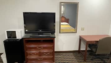 A hotel room with a television, a microwave, a wooden dresser, a desk, and two beds.