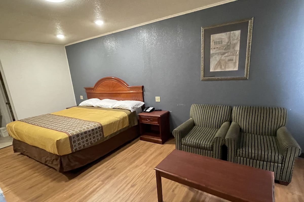 A hotel room with a bed, a striped armchair, a wooden nightstand, and a small table.