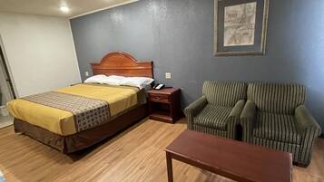 A hotel room with a bed, a striped armchair, a wooden nightstand, and a small table.