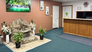 A reception area with a reception desk, a ceiling fan, a wall-mounted clock, and a waterfall painting. - Sallisaw Inn (Sallisaw)