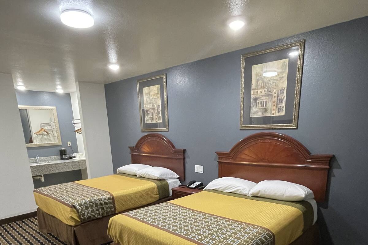 A hotel room with two beds, a bathroom, and a patterned carpet.