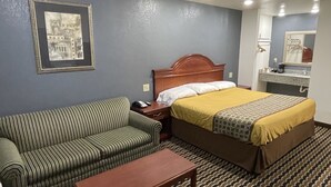 A hotel room with a bed, a green striped sofa, a wooden nightstand, and a small table. - Sallisaw Inn (Sallisaw)