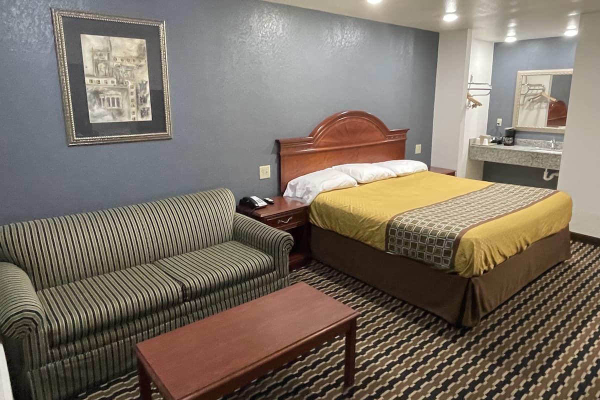 A hotel room with a bed, a green striped sofa, a wooden nightstand, and a small table.