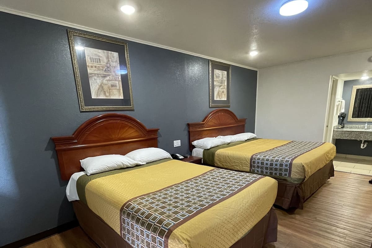 A hotel room with two beds, wooden headboards, and a bathroom with a sink and mirror.
