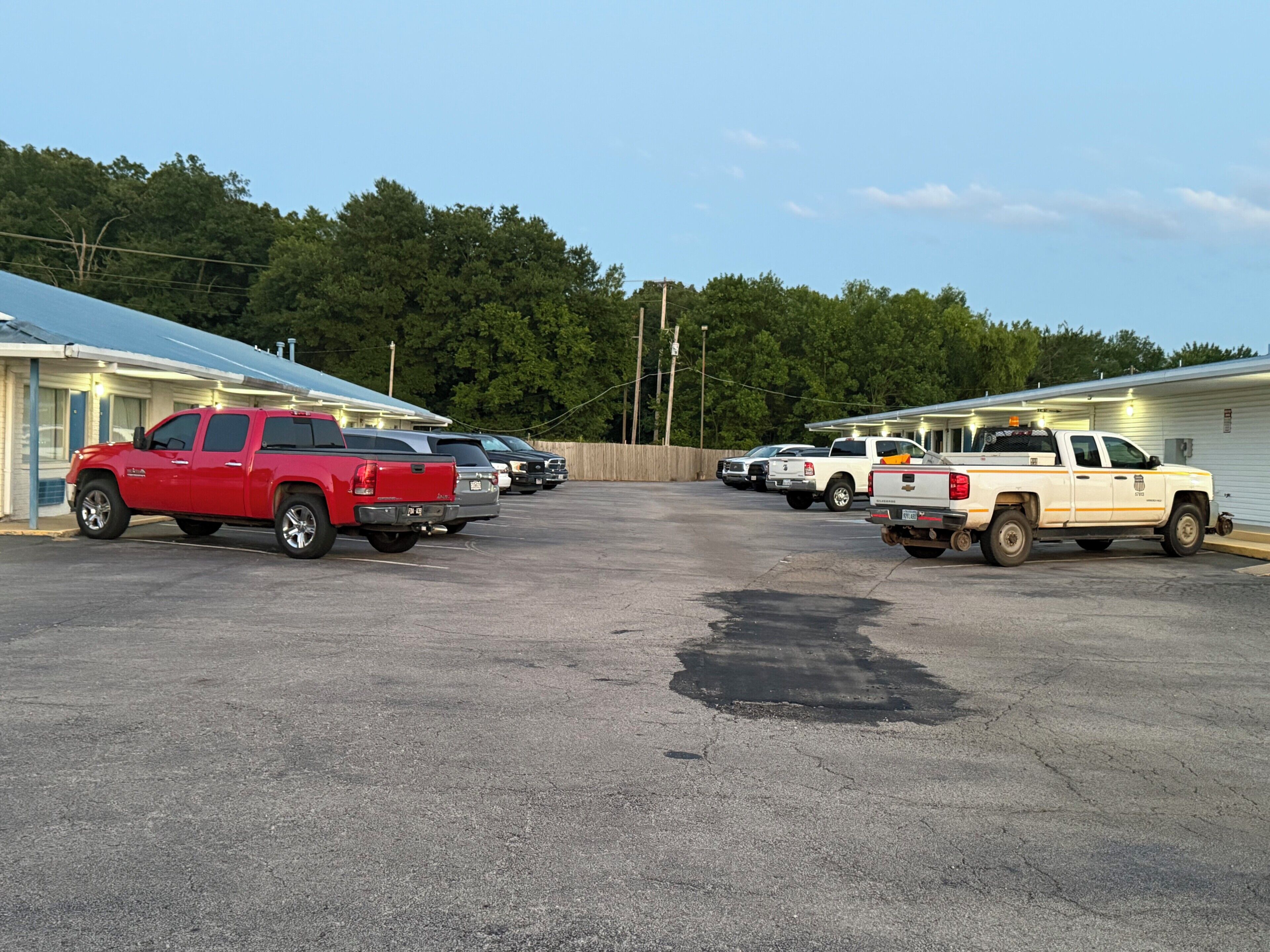 A parking lot with several pickup trucks, a building with a blue roof, and trees in the background.