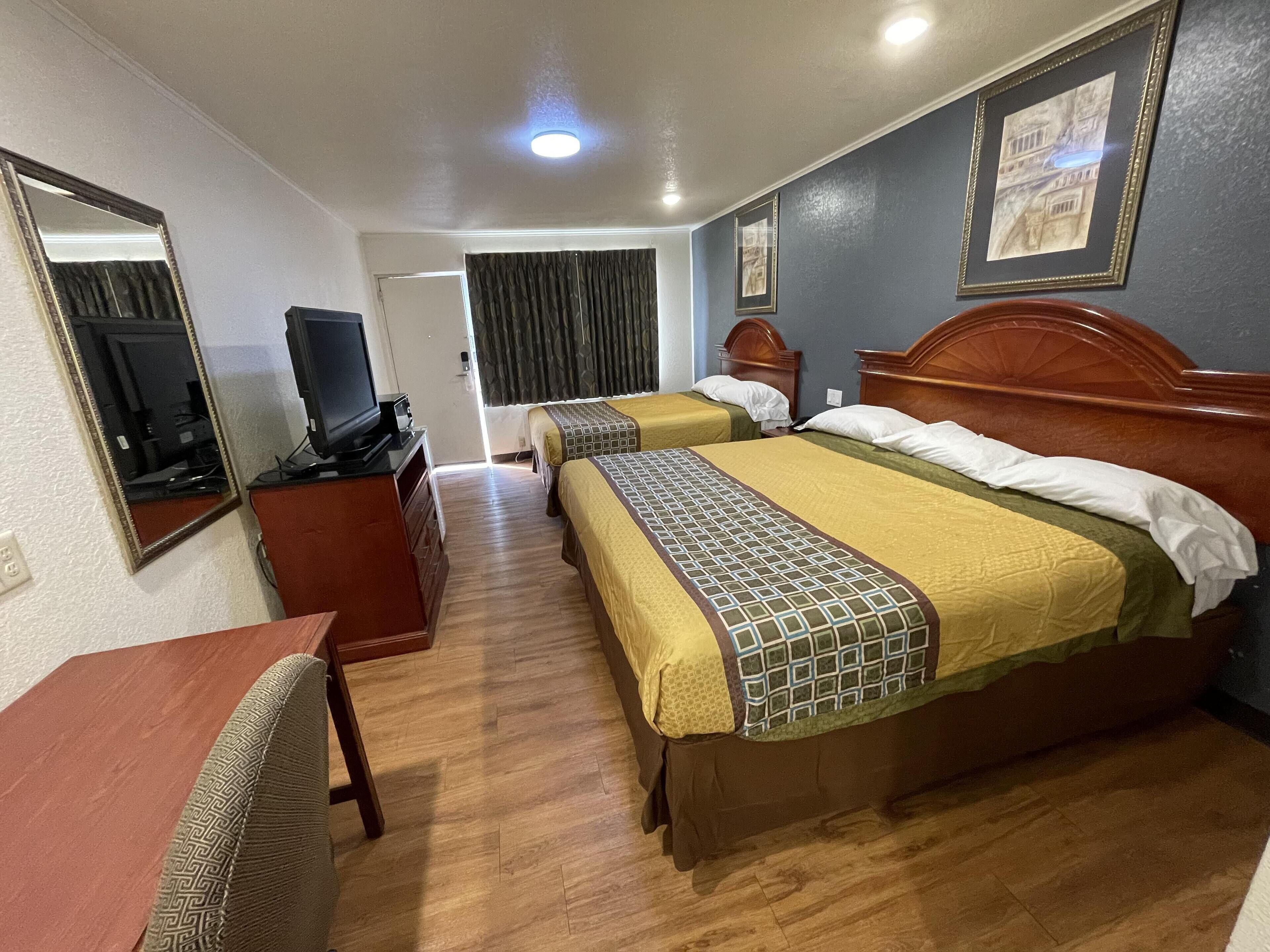 A hotel room with two beds, a desk, a television, and a mirror.