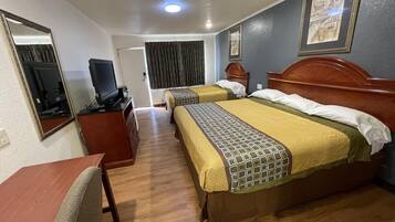 A hotel room with two beds, a desk, a television, and a mirror.