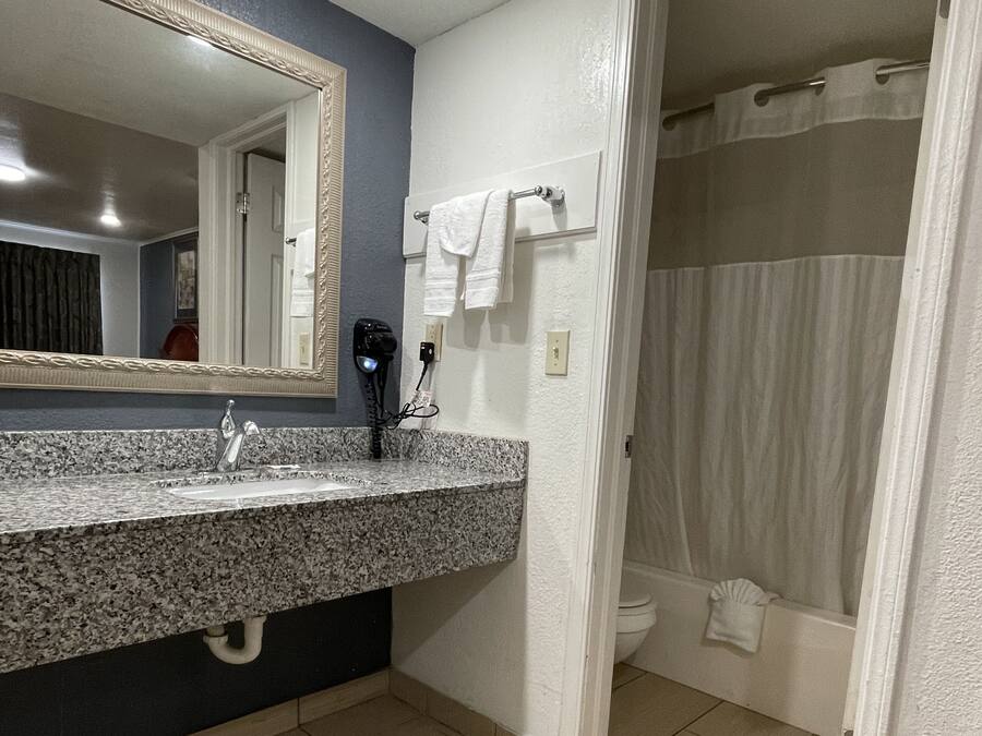A bathroom with a granite countertop, a mirror, a hairdryer, and a shower curtain.