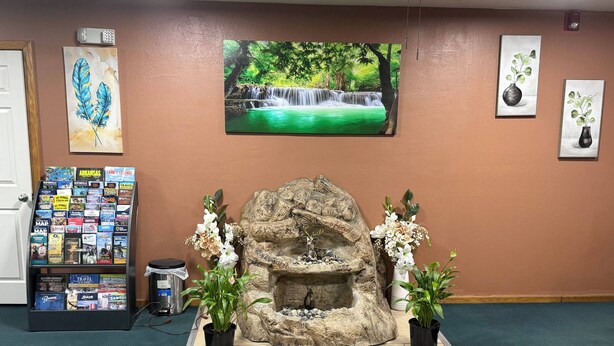 A reception area with a stone fountain, potted plants, travel brochures, and framed artwork on the wall. - Sallisaw Inn (Sallisaw)