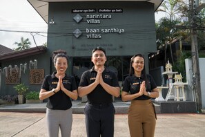 Tres personas de pie frente a un edificio con un cartel que dice 'Narintara Villas' y 'Baan Santhiya Villas'.