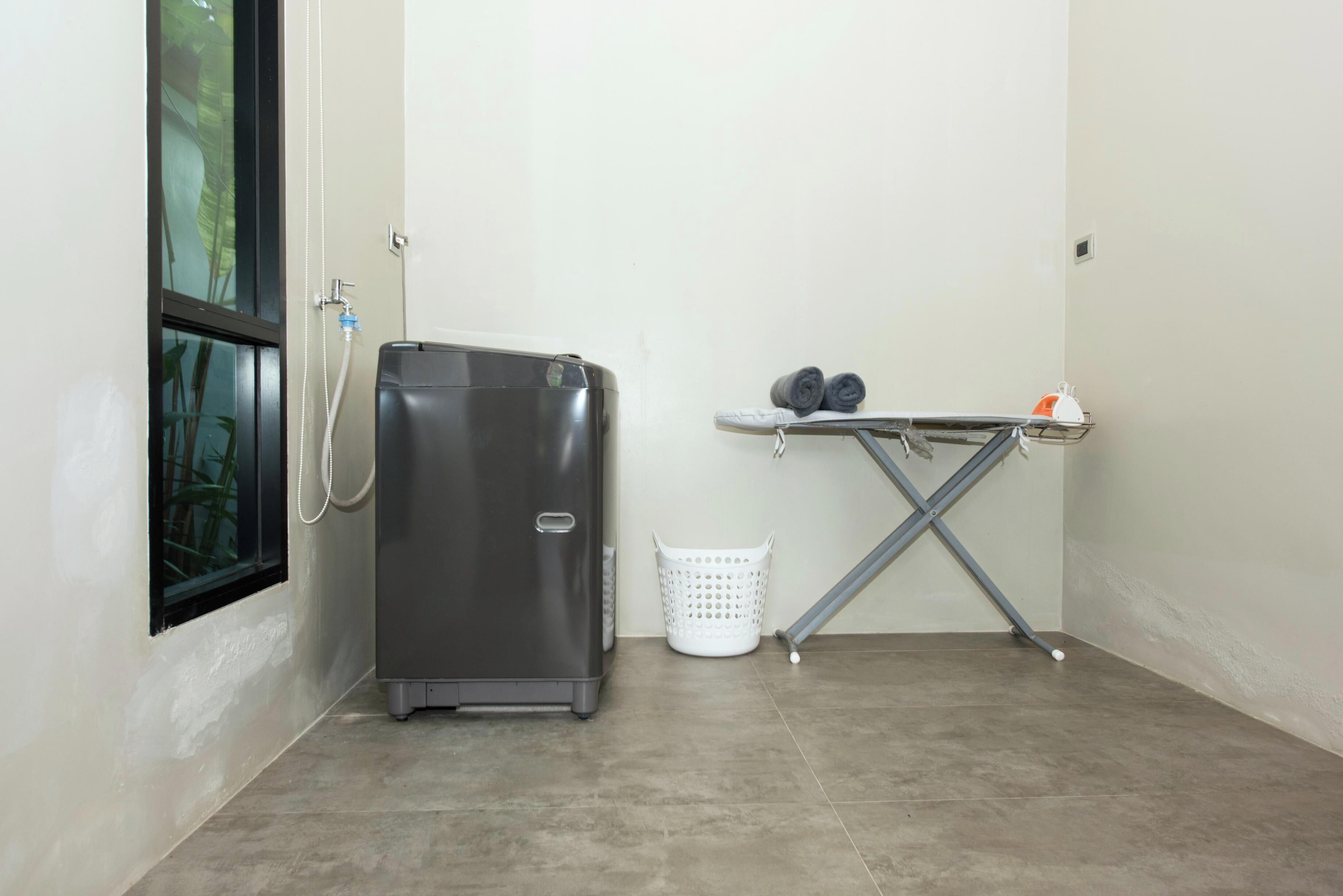 A compact room with a water dispenser, a laundry basket, and an ironing board.