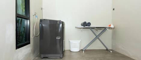 A compact room with a water dispenser, a laundry basket, and an ironing board.