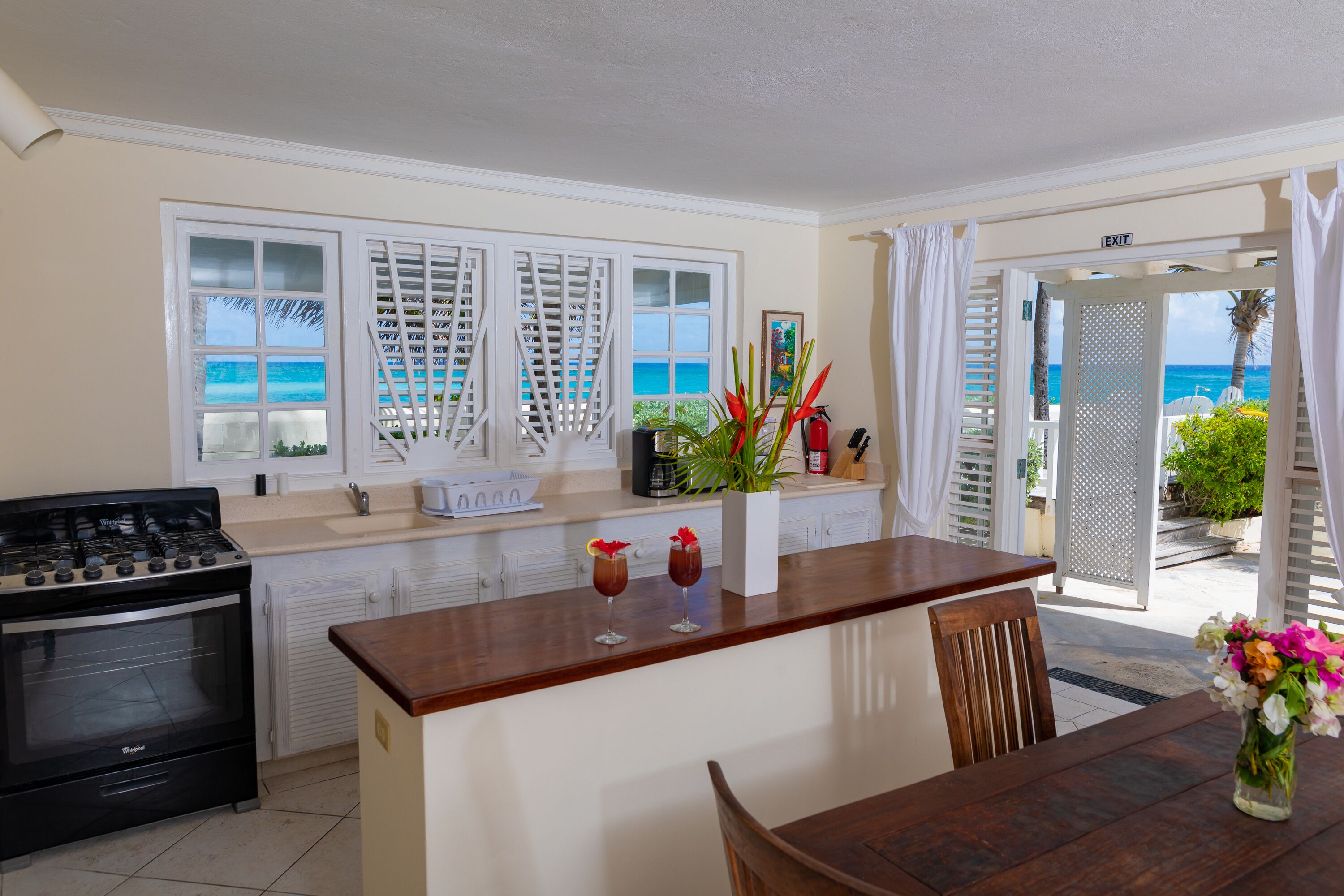 A kitchen with a stove, a dining area with a table and chairs, and a view of the ocean through the windows.
