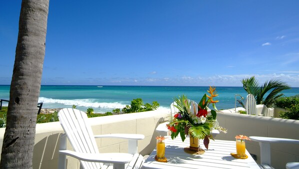 Mesa con dos sillas y un centro de mesa floral, con vista a una playa y un cielo azul despejado.