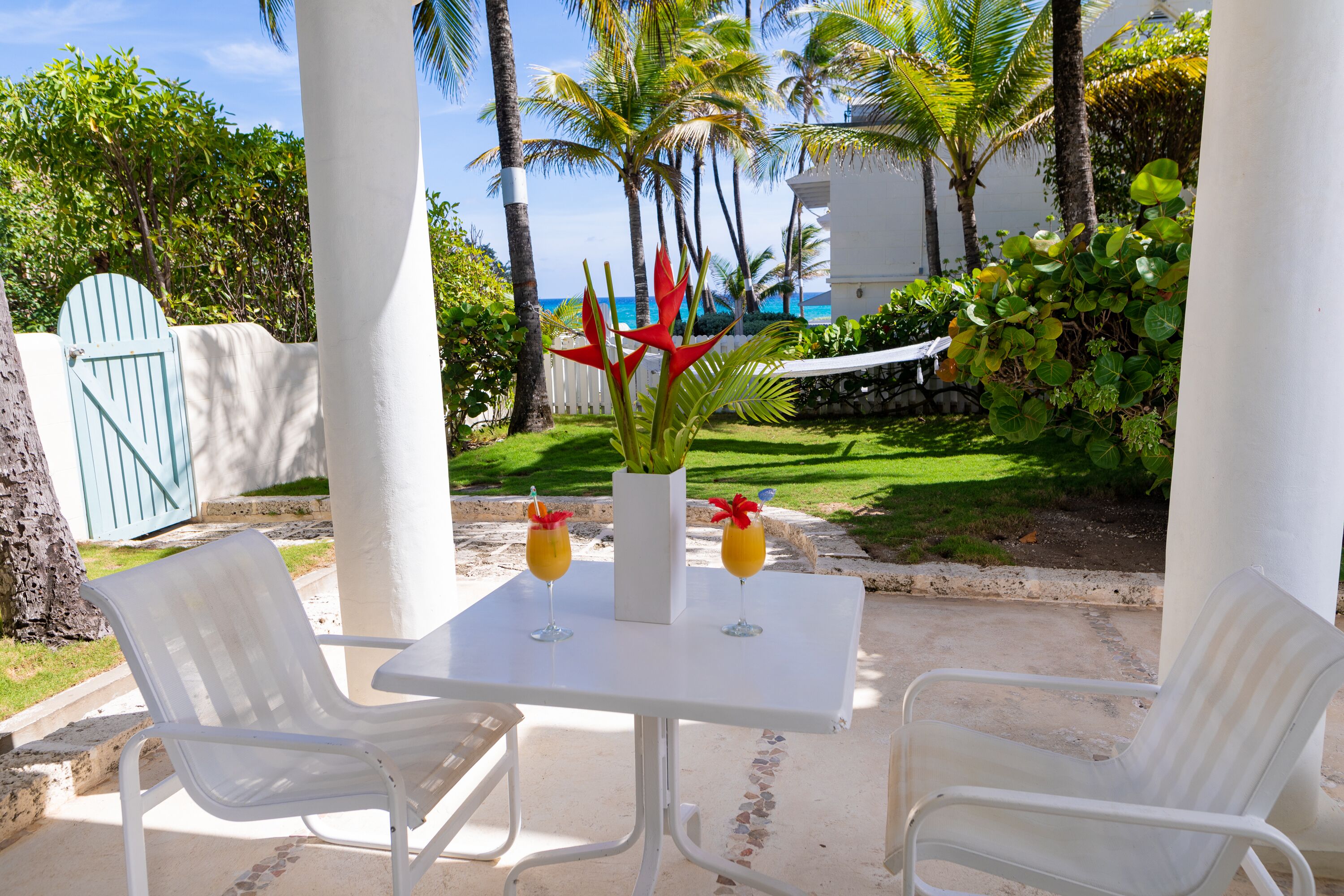 A white table with two chairs, a white pillar, and a view of the ocean and palm trees.