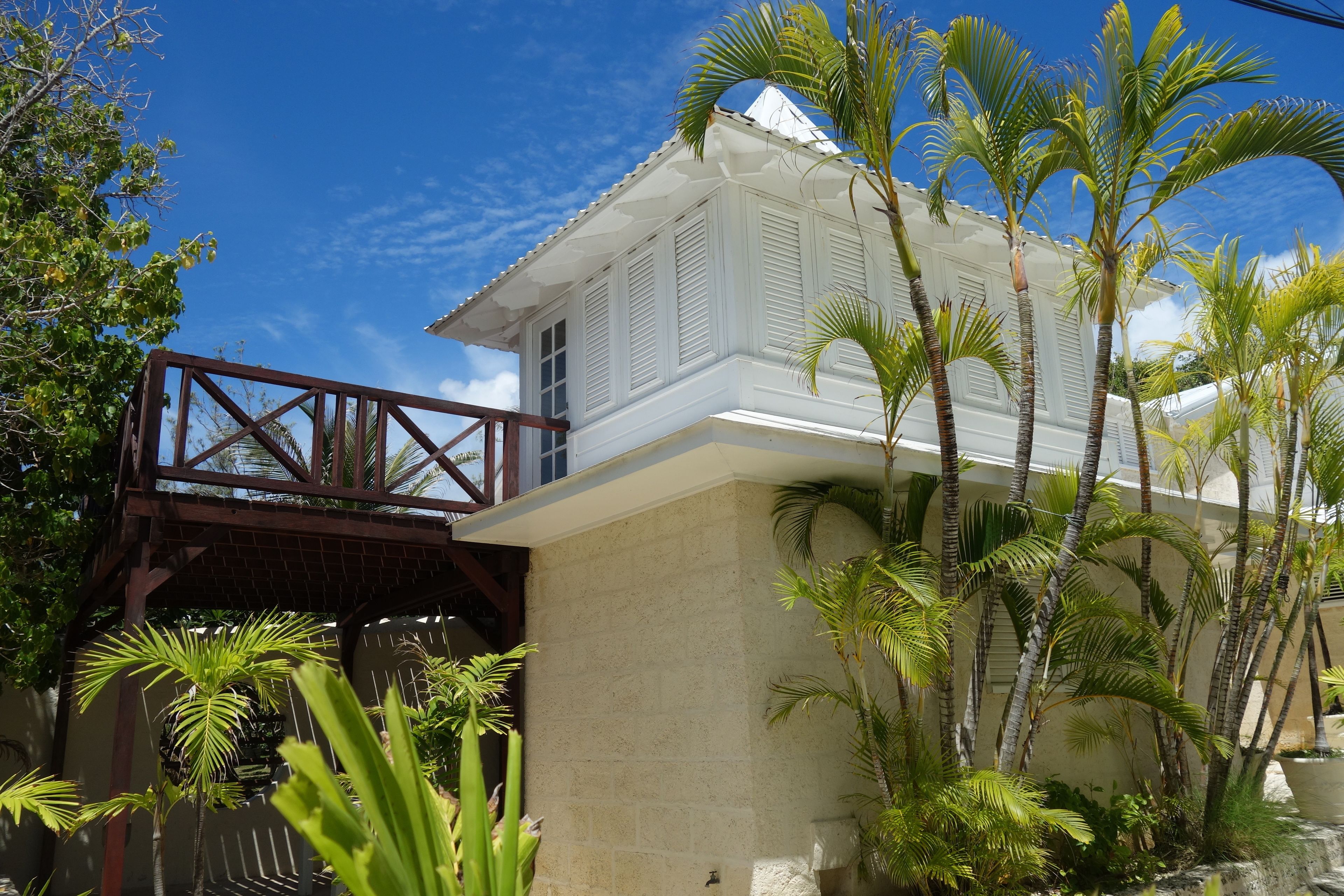 A white colonial-style building with a balcony, surrounded by palm trees and a wooden bridge. - Inchcape Seaside Villas (Silver Sands)