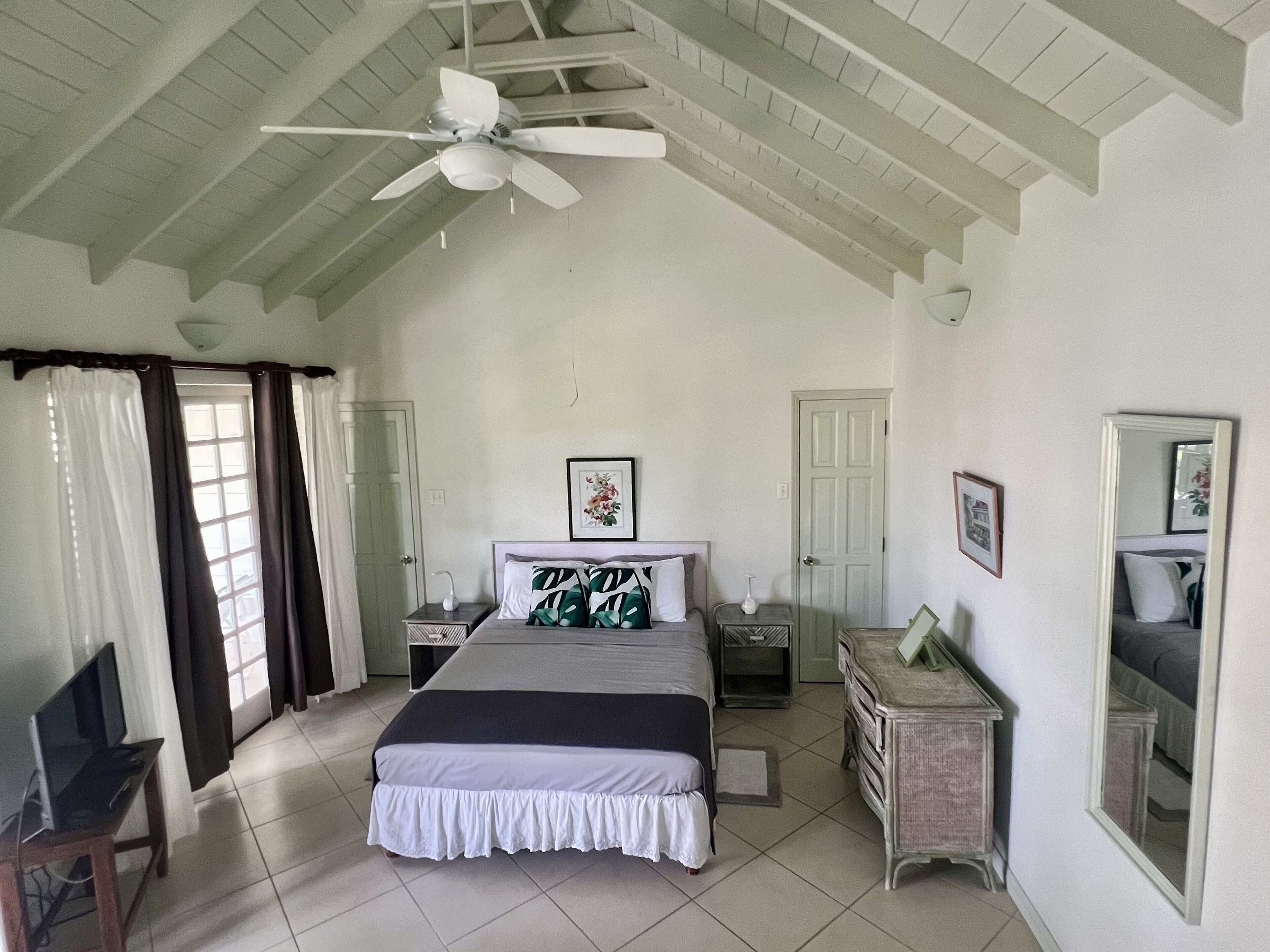 A bedroom with a bed, a nightstand, a dresser, a ceiling fan, and a window with curtains.