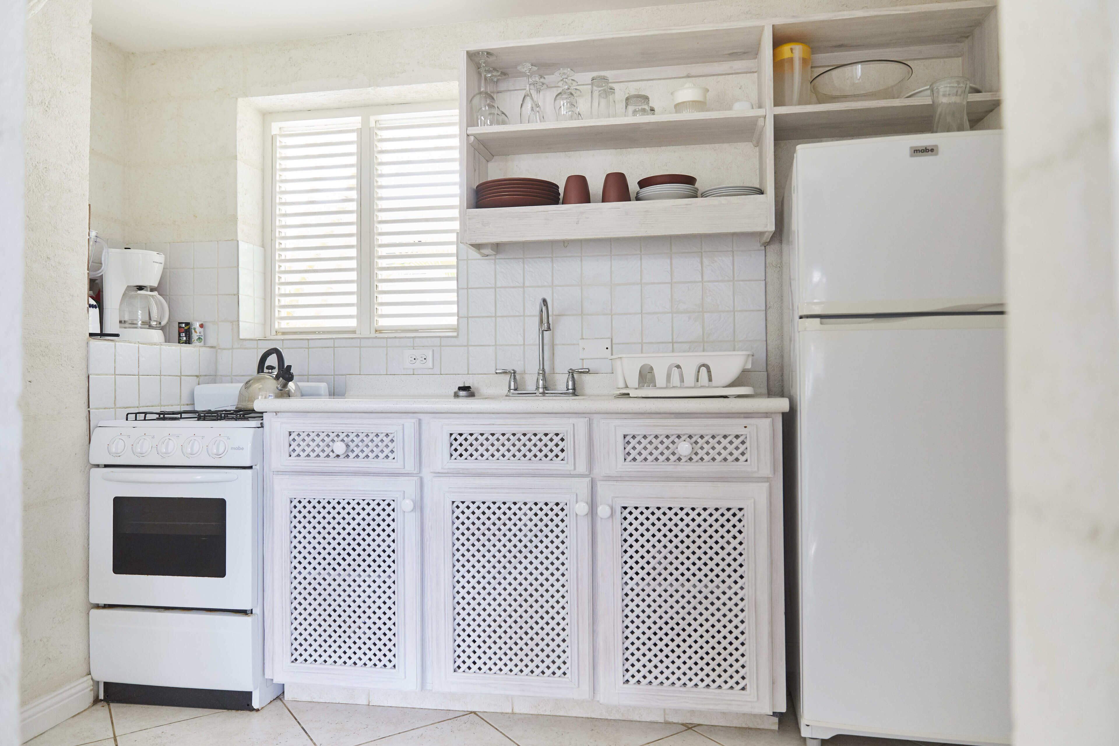 Una cocina con muebles blancos, estufa, pileta y refrigerador.