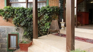 Un edificio de ladrillo con un acceso con tejas, una silla de madera y una planta en maceta.