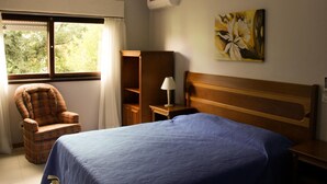 Un dormitorio con cama, una silla, un escritorio y un cuadro en la pared.
