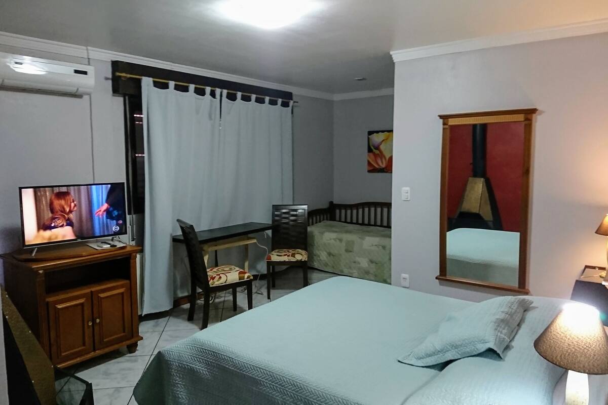 A hotel room with a bed, a desk, a chair, a television, and a lamp.
