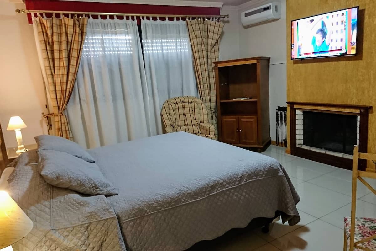 A bedroom with a bed, a chair, a TV, a wardrobe, and a fireplace.