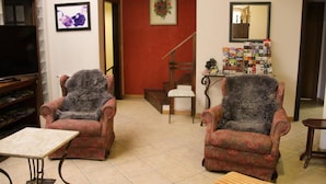 Una sala de estar con dos sillones estampados, una mesita, una estantería, un televisor y una escalera.
