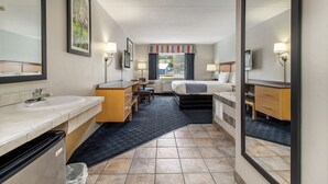 A hotel room with a bathroom, a desk, a bed, and a window with curtains.