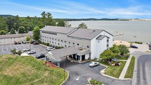 A hotel with a parking lot, a covered entrance, and a view of a large body of water.