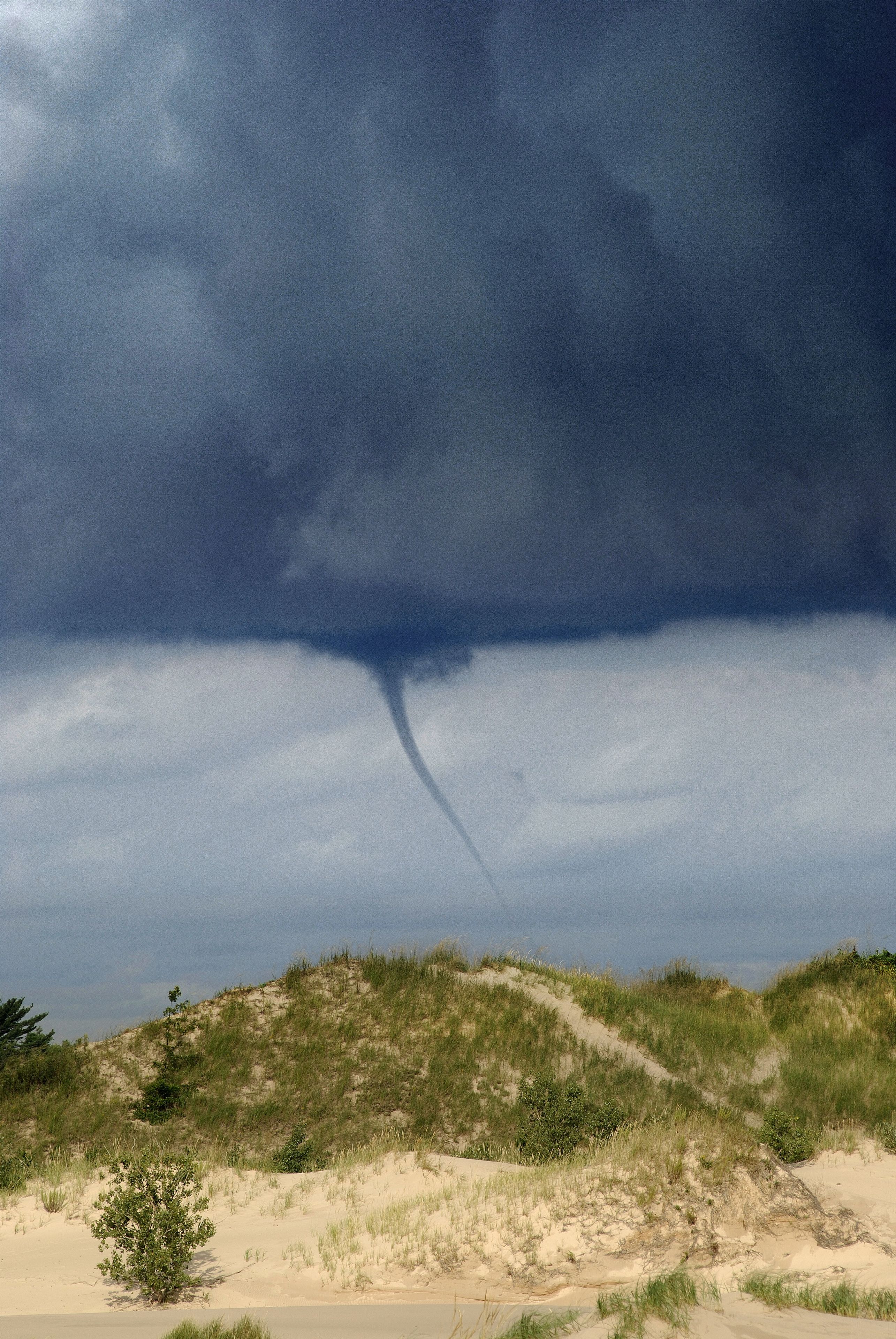 A landscape with sand dunes and a tornado funnel.