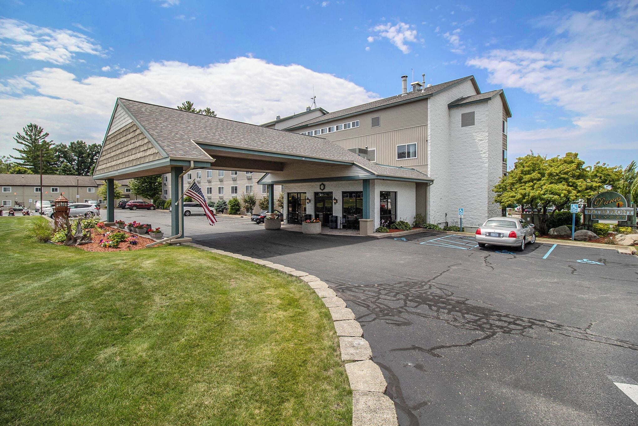 Ein Hotel mit überdachter Einfahrt, Parkplatz und bepflanztem Bereich mit Blumen.