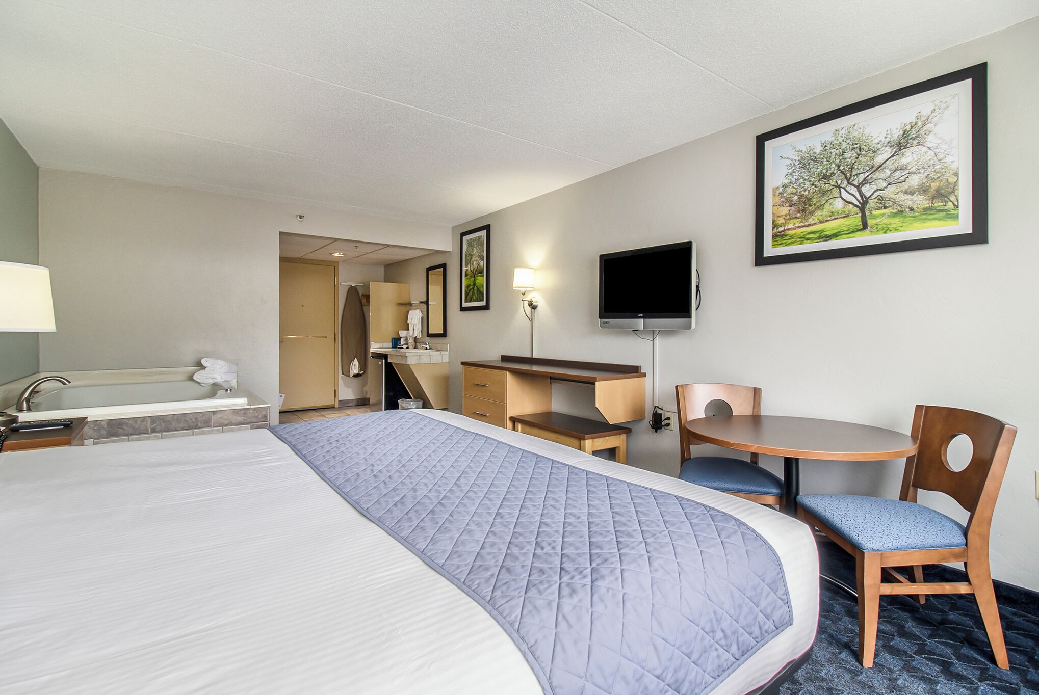 A hotel room with a large bed, a desk with a chair, a television, and a bathroom with a bathtub.