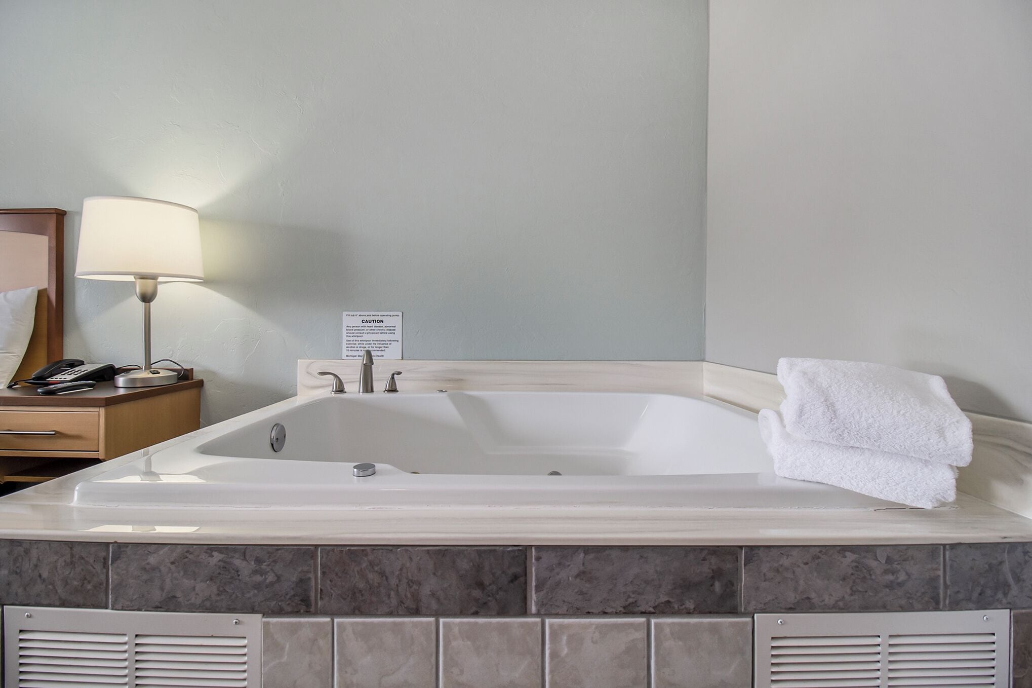 Une salle de bain avec une grande baignoire, une table de chevet avec une lampe et une serviette à proximité.