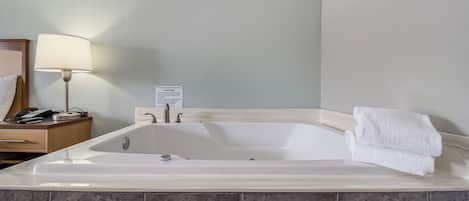 Une salle de bain avec une grande baignoire, une table de chevet avec une lampe et une serviette à proximité.