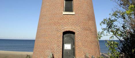 A tall brick lighthouse with a circular base and a narrow top, featuring a small window and a door at the base.