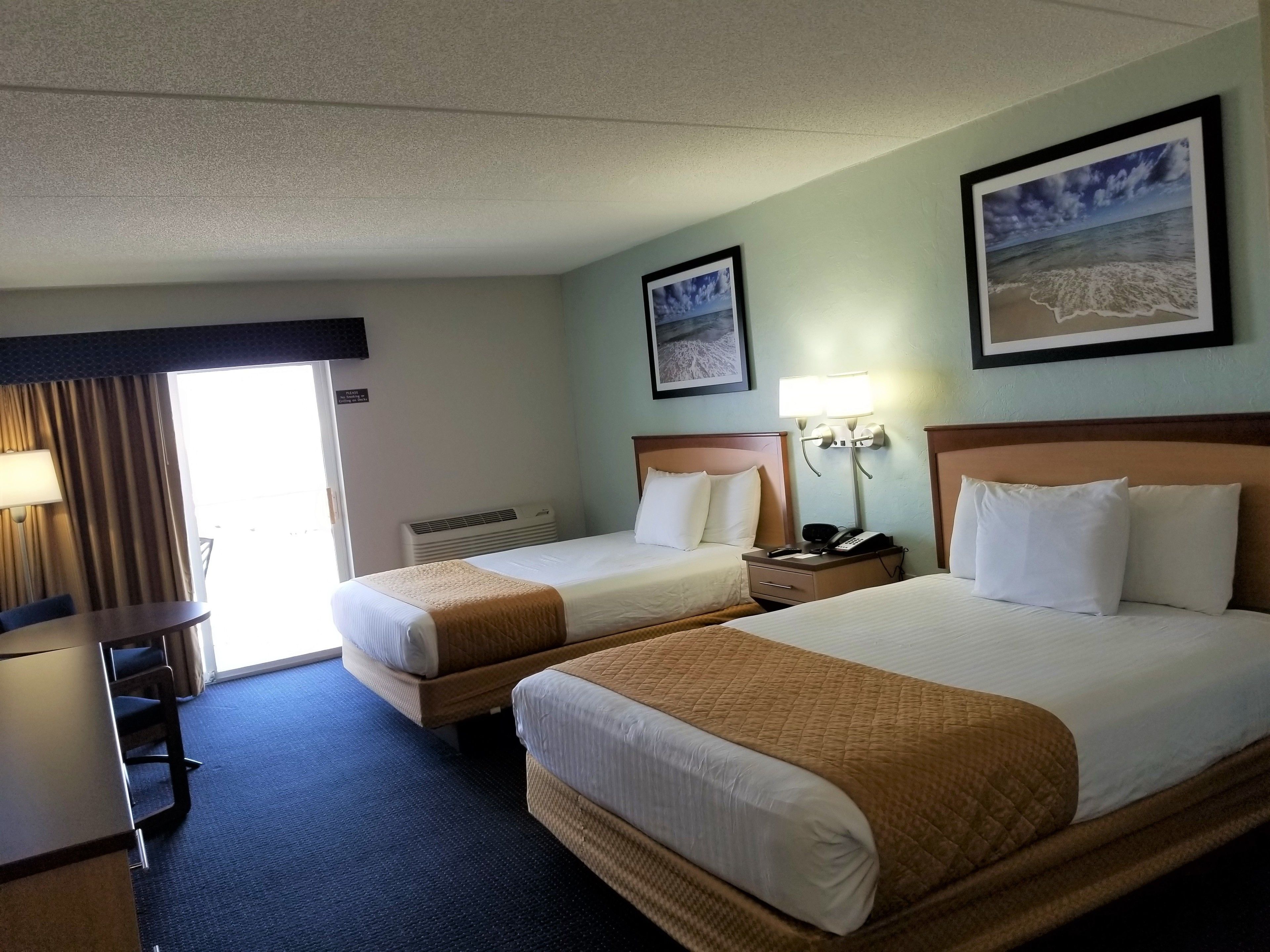 A hotel room with two beds, a desk, a chair, a lamp, a phone, and a framed picture on the wall.