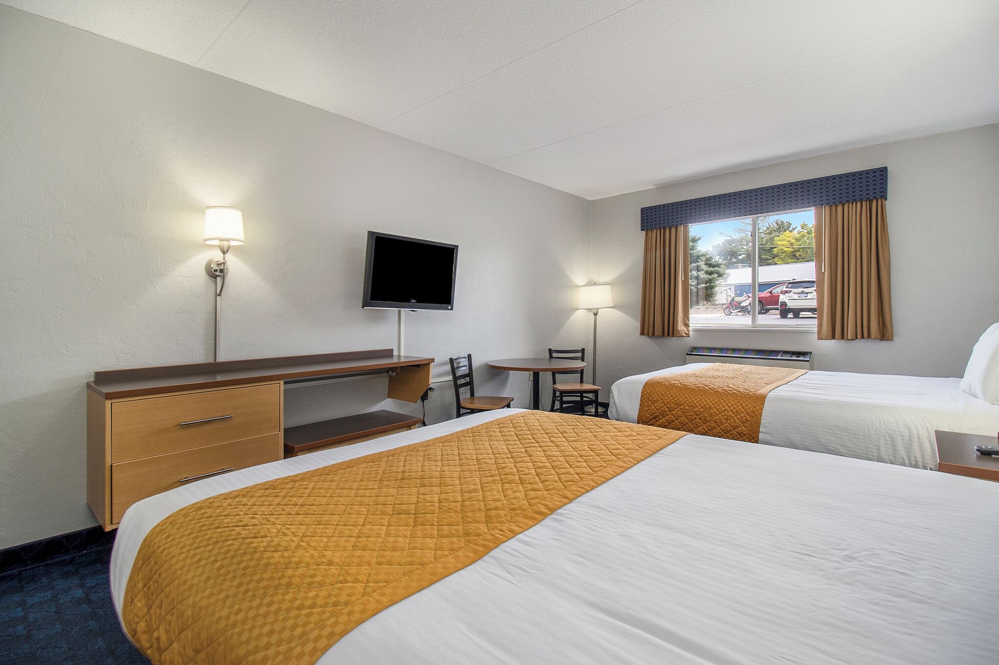 Una habitación de hotel con dos camas, un escritorio, una silla, un televisor y una ventana con cortinas.