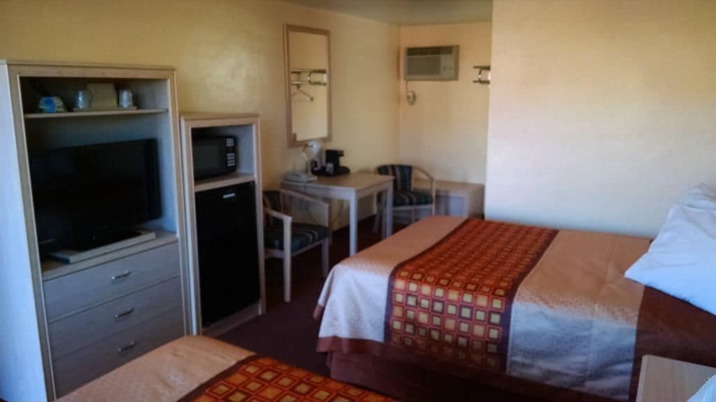 A hotel room with two beds, a desk, a chair, a television, and a microwave.