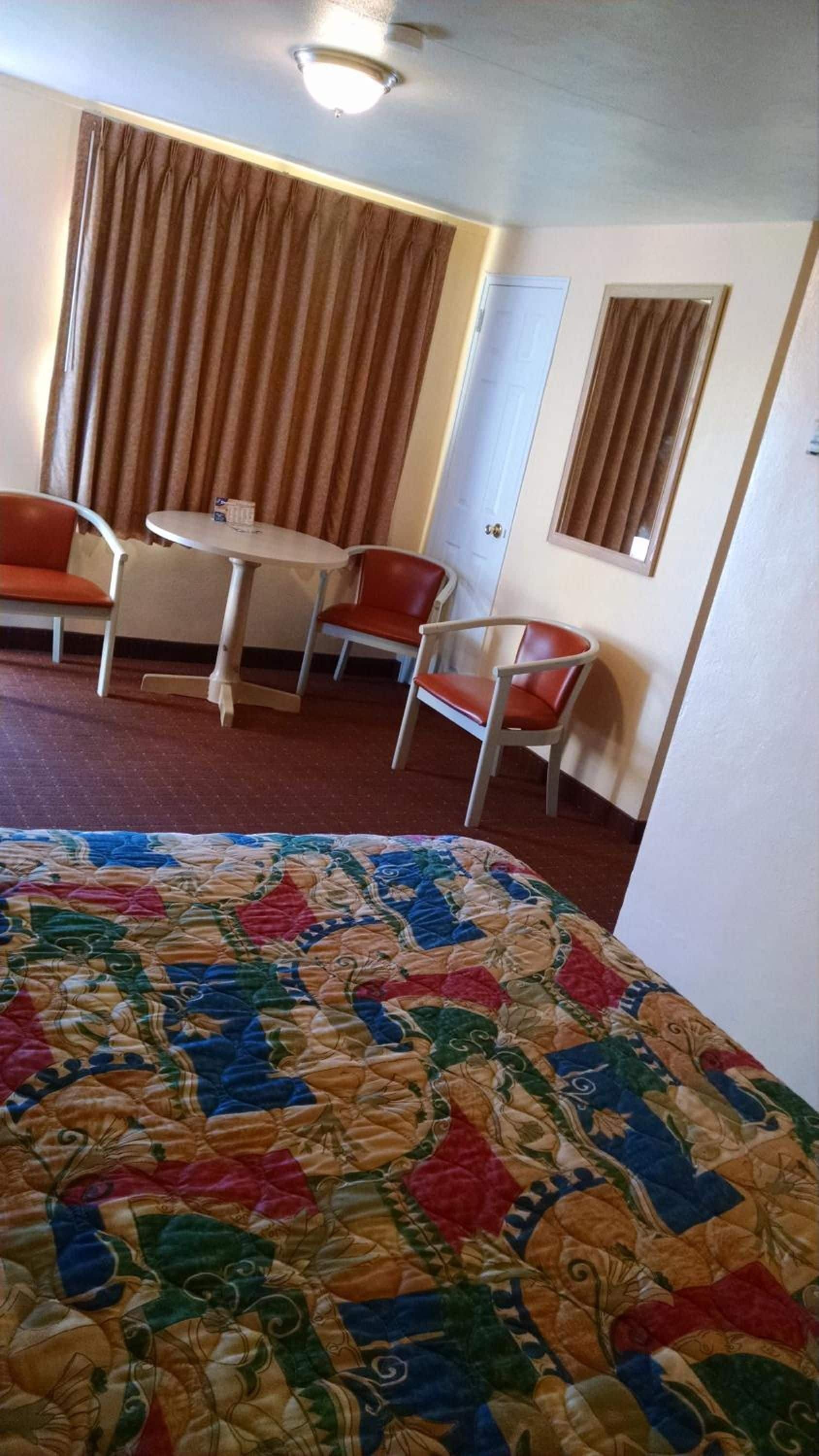 A hotel room with a bed, a table, two chairs, and a door.