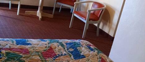 A hotel room with a bed, a table, two chairs, and a door.