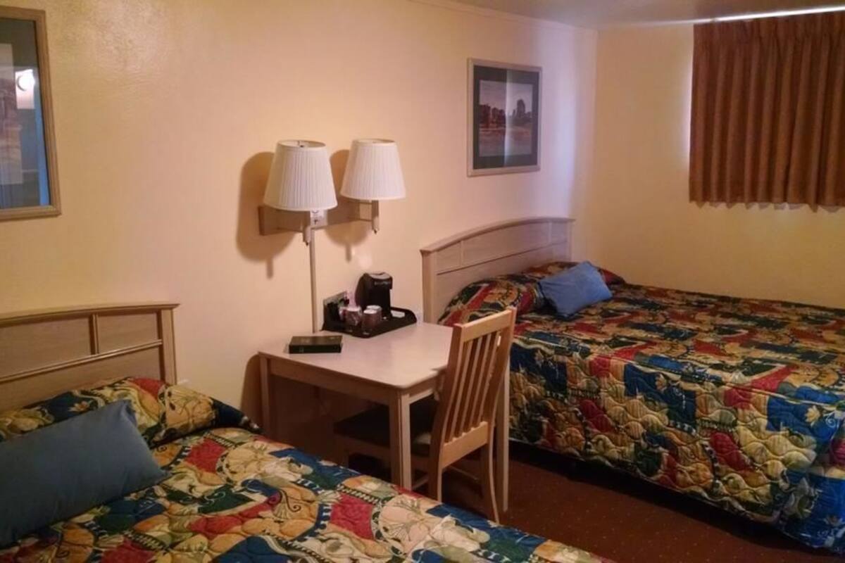 A hotel room with two single beds, a small table with a chair, a desk with a lamp, and a coffee maker.